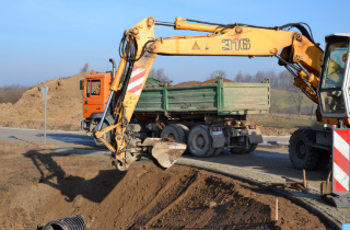 Photo of an excavator digging a ditch on the side of a roadway 