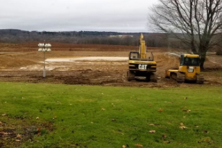 Photo of an excavator and bulldozer sitting in front of an unfinished pond